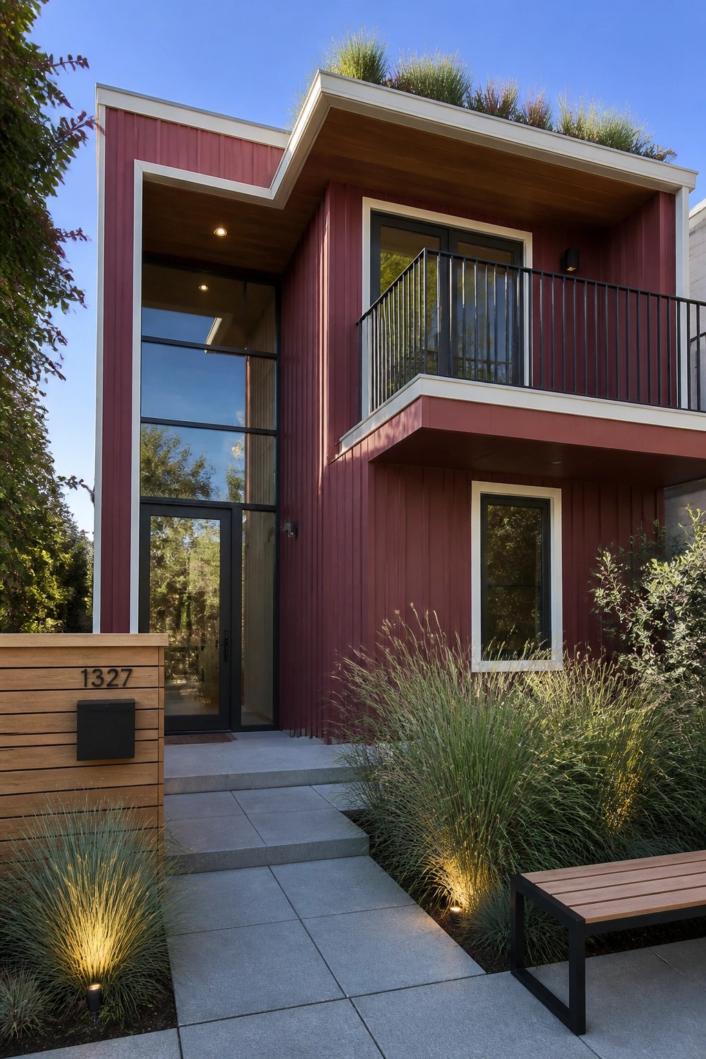A two-story modern house with burgundy vertical siding, warm white trim, a black-railed balcony, and tall glass windows beside the front door.