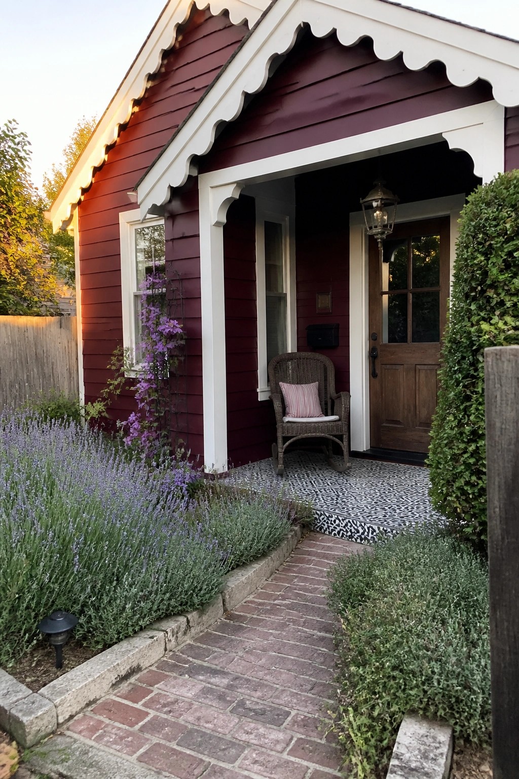 Red cottage porch with wicker chair, wooden door, brick path, and lavender garden