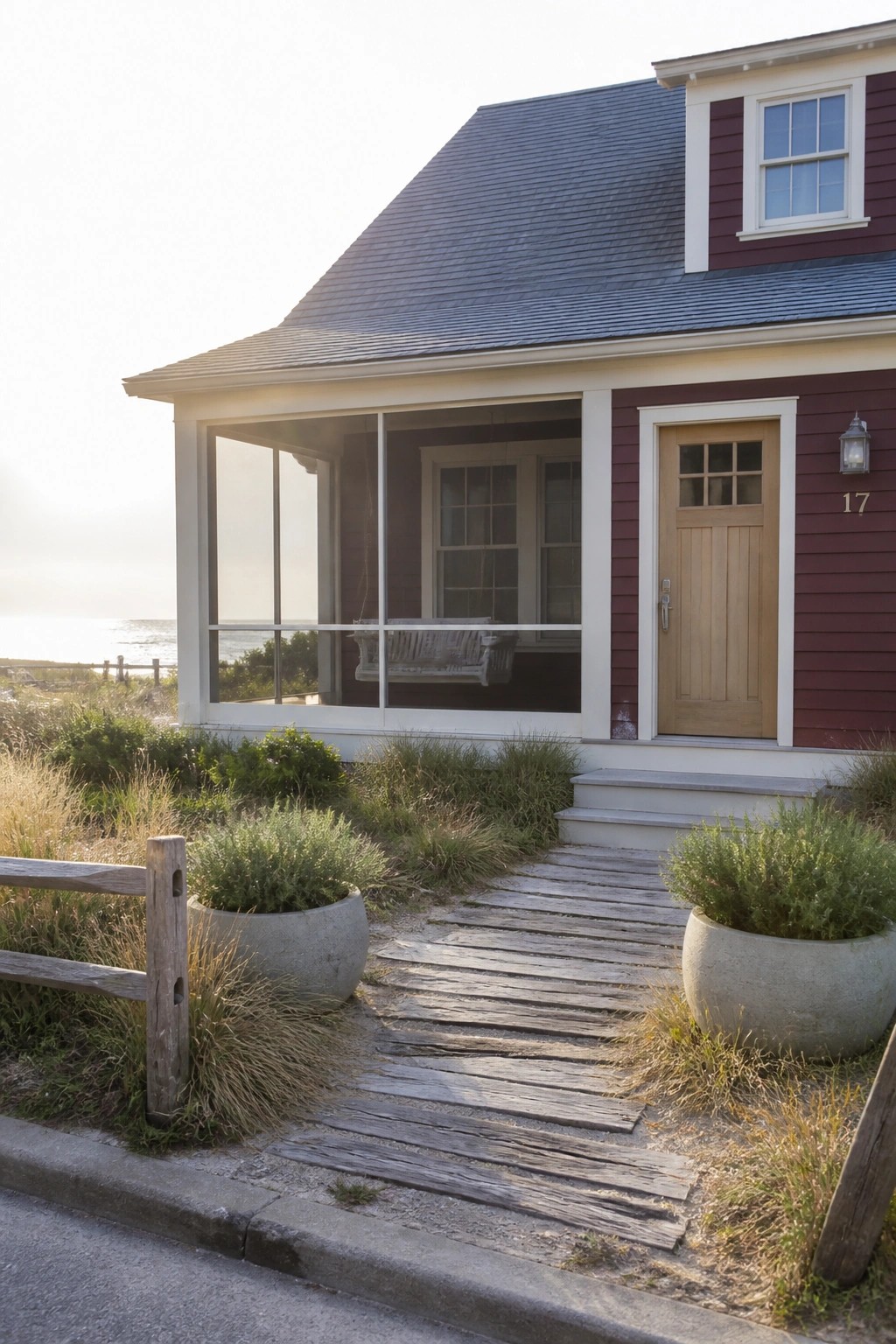 A burgundy house with white trim shows a wooden front door, screened porch, and wooden walkway with potted plants beside it.
