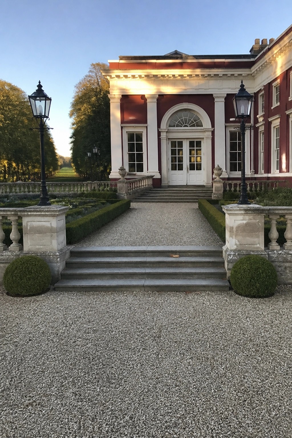 Grand red-brick mansion with white columns, steps, and gravel path at dusk.