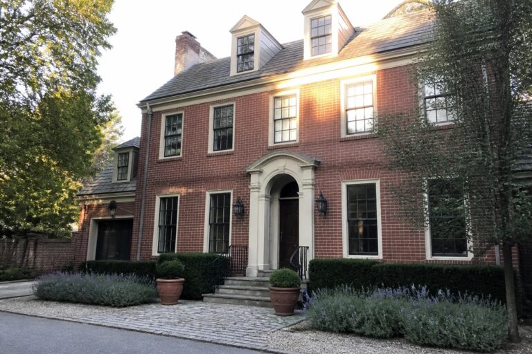 22 Elegant Burgundy House Exteriors Paired with Warm White Trim A two-story red brick house with white trim around the arched front entry, windows, and dormers, shown from the front with steps and landscaping.