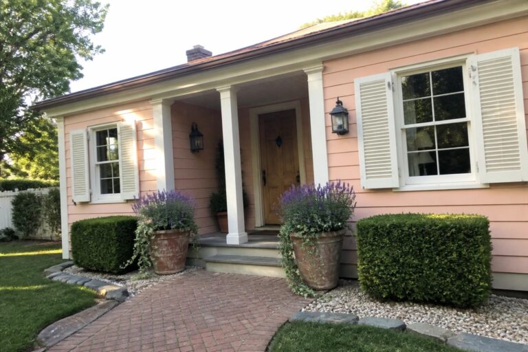 21 Fresh Peach House Exteriors Featuring Crisp White Shutters Peach house with white porch, brick path, potted purple flowers, and green shrubs.