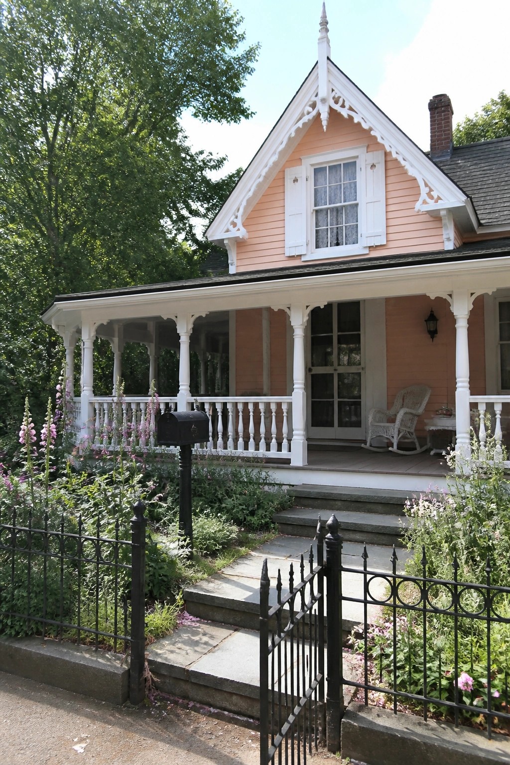 Peach Victorian house with white porch, rocking chair, black fence, and garden flowers.