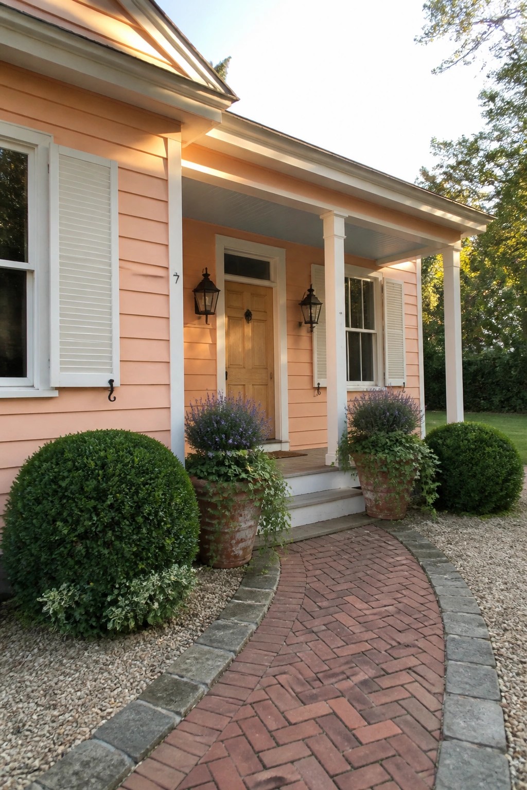 Peach house with white porch, brick path, potted purple flowers, and green shrubs.