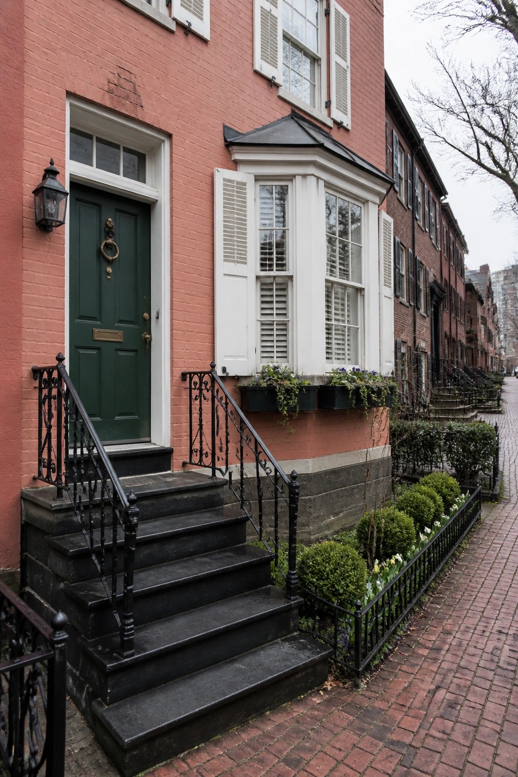 Red brick townhouse with green door, black stairs, and white bay window.