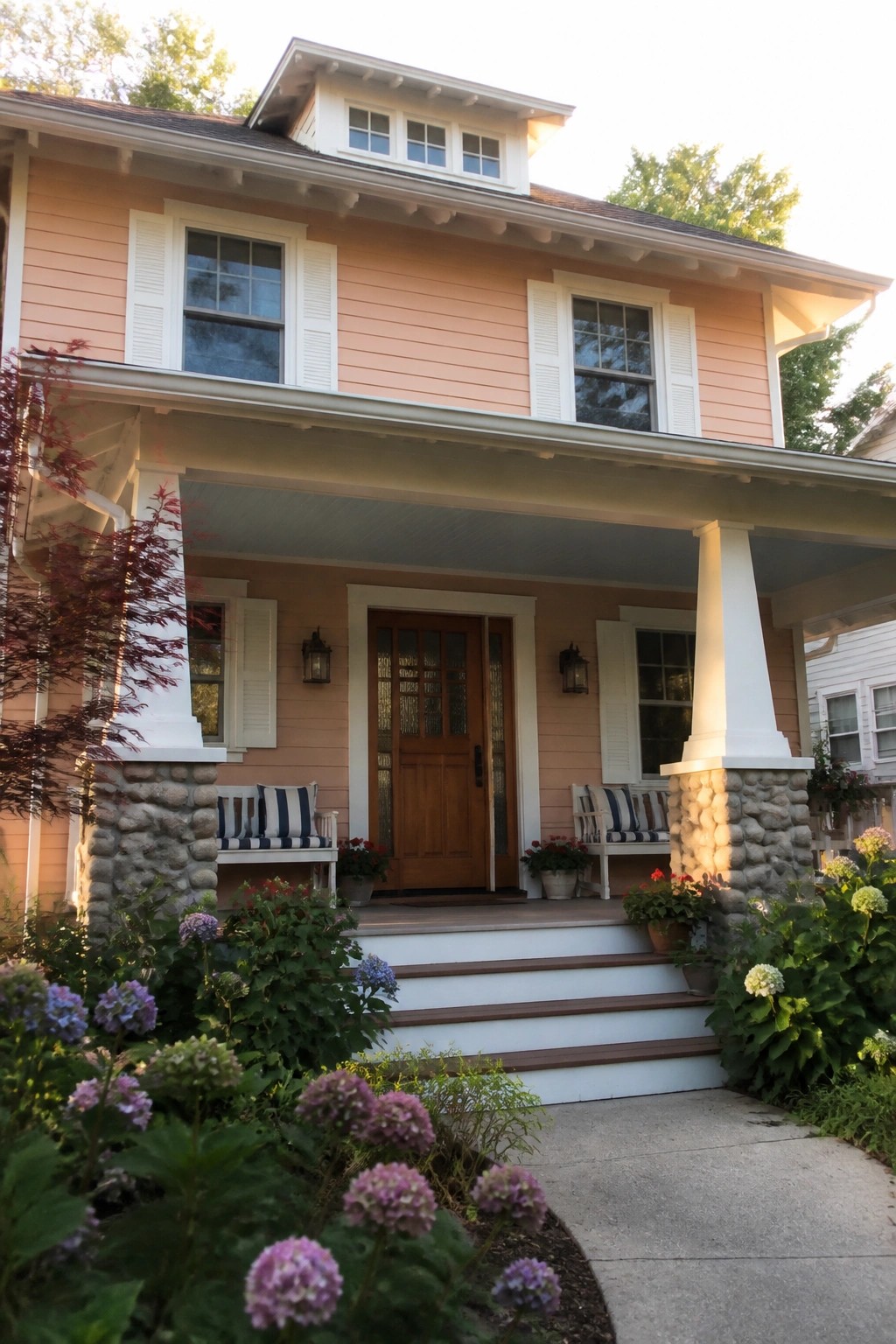 Peach two-story house with white porch columns, wooden door, and blooming hydrangeas.