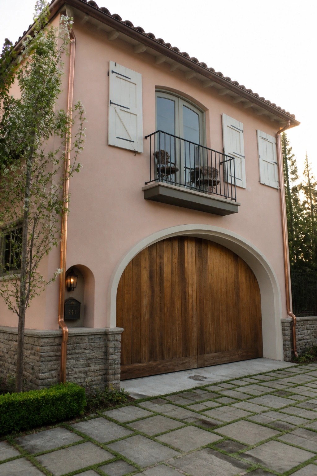 A two-story peach stucco house with white shutters, a wooden arched garage door, and a small balcony with black railing.
