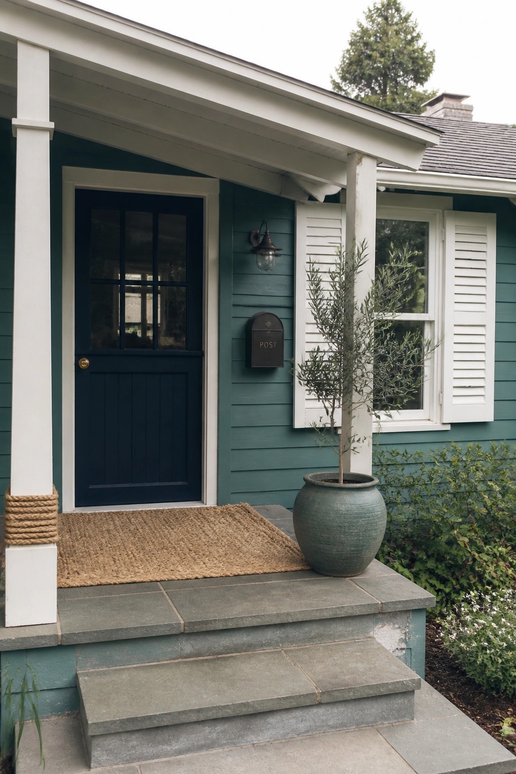 Teal house porch with navy door, white shutters, potted tree on stone steps.