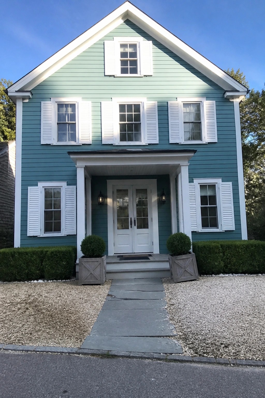 Light green two-story house with white shutters, double doors, and gravel path