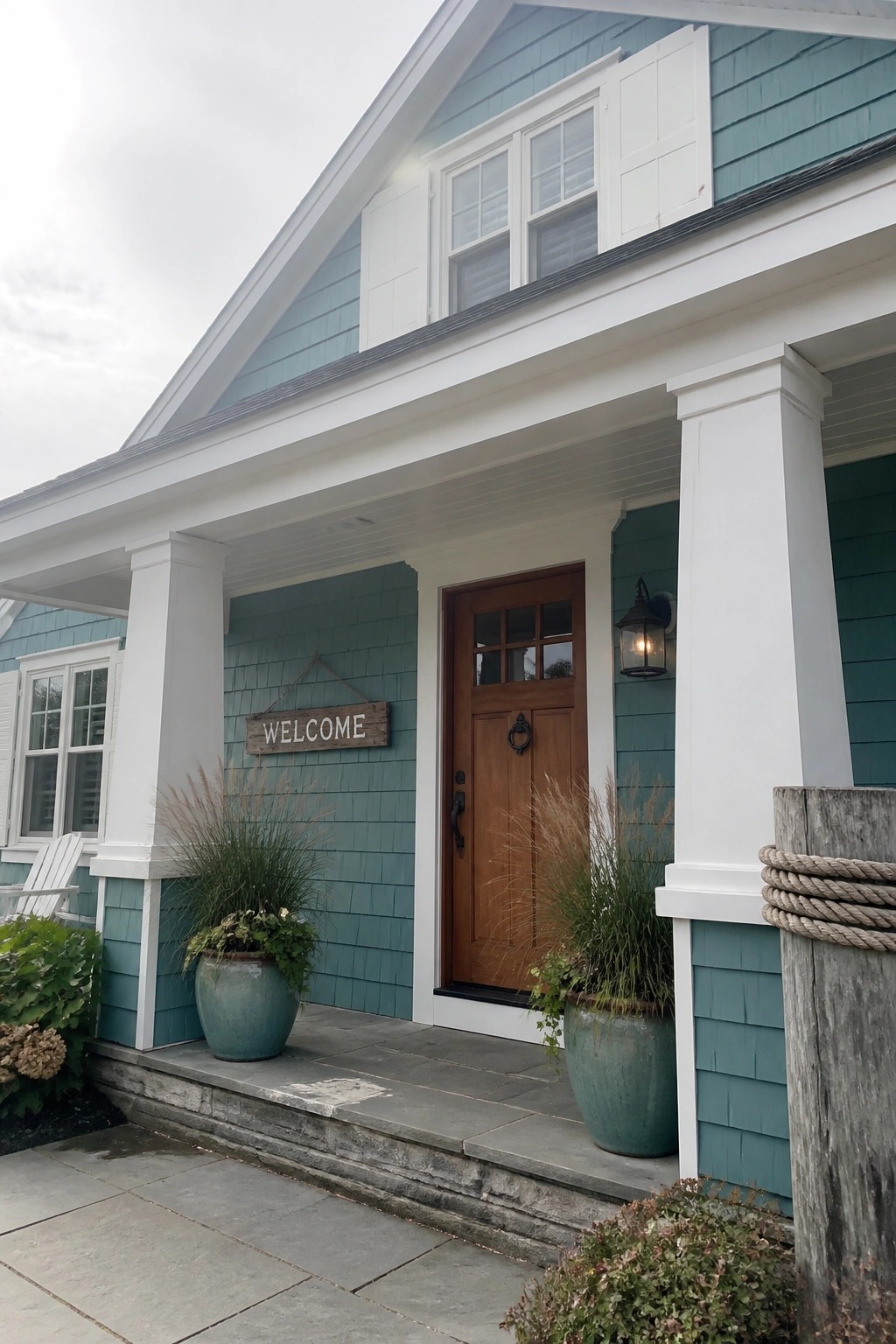 Teal shingled house porch with wooden door, welcome sign, and potted plants
