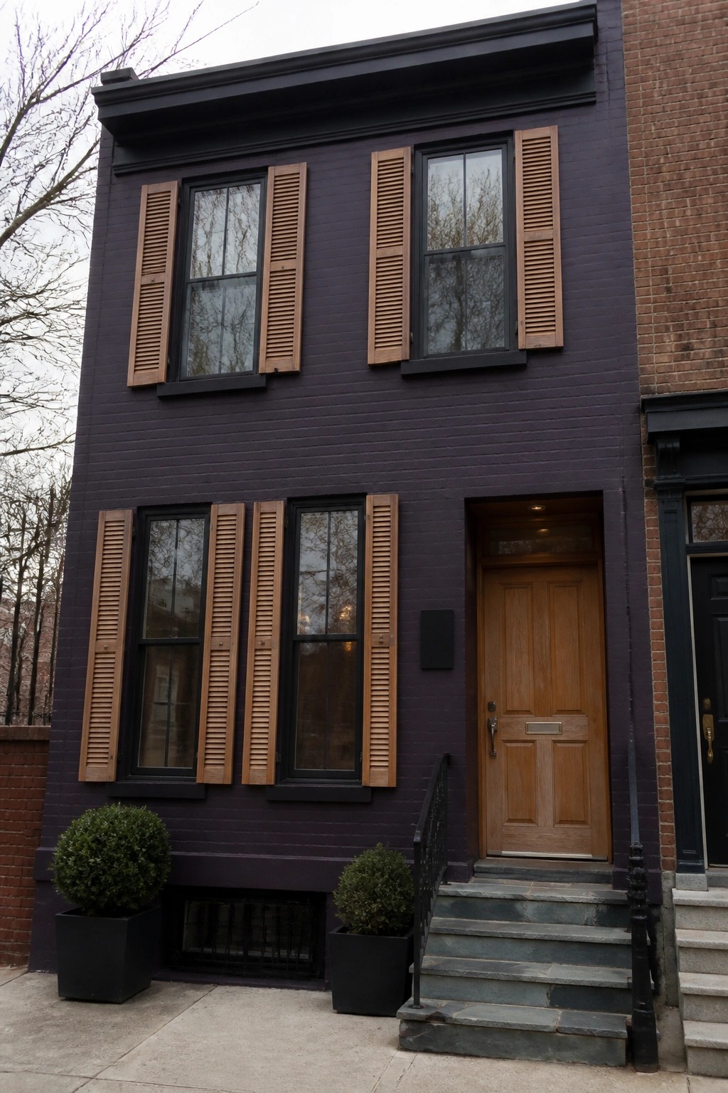Dark purple brick townhouse with wooden shutters, door, and stone steps.