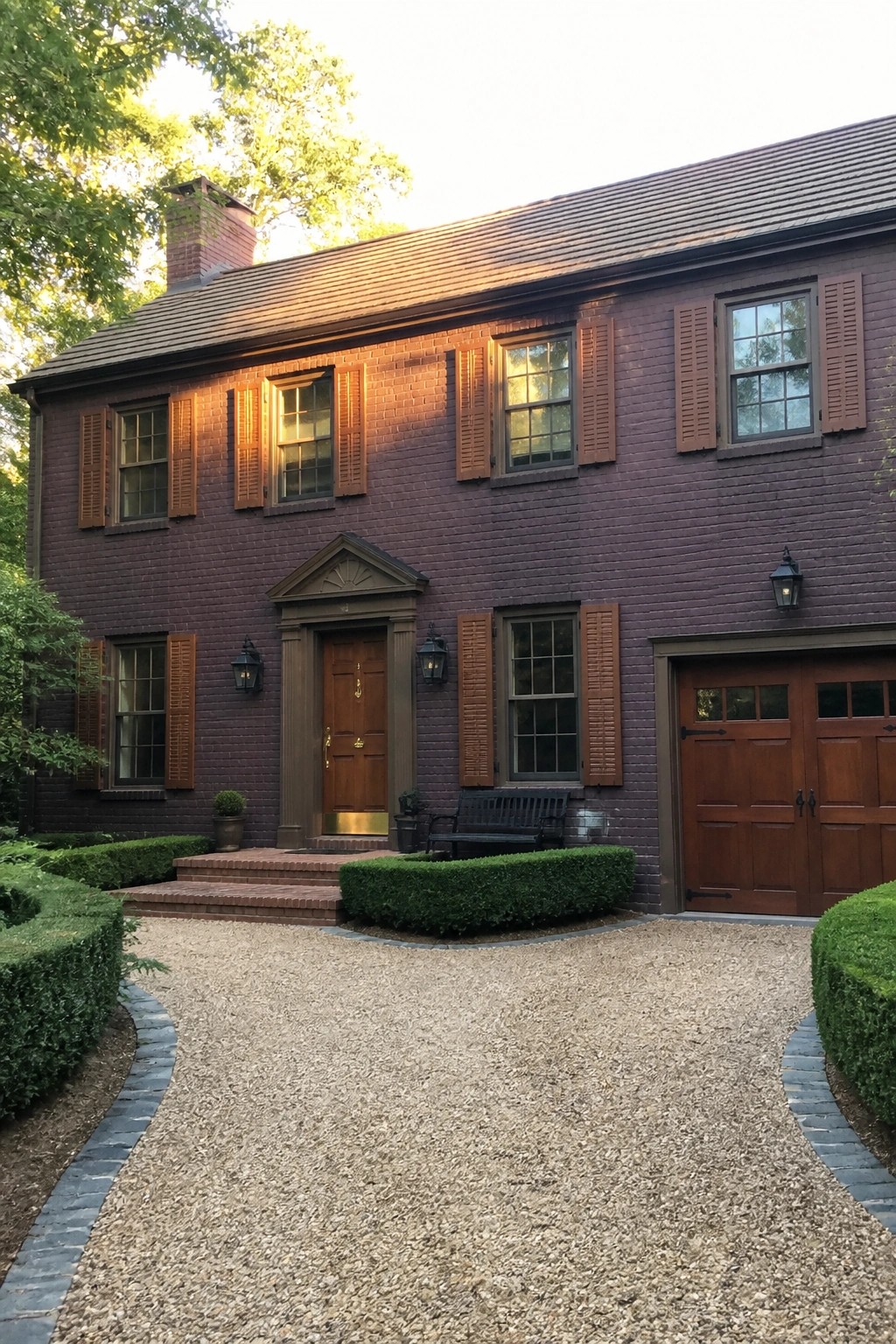 Purple brick colonial house with brown shutters, wooden door and gravel driveway