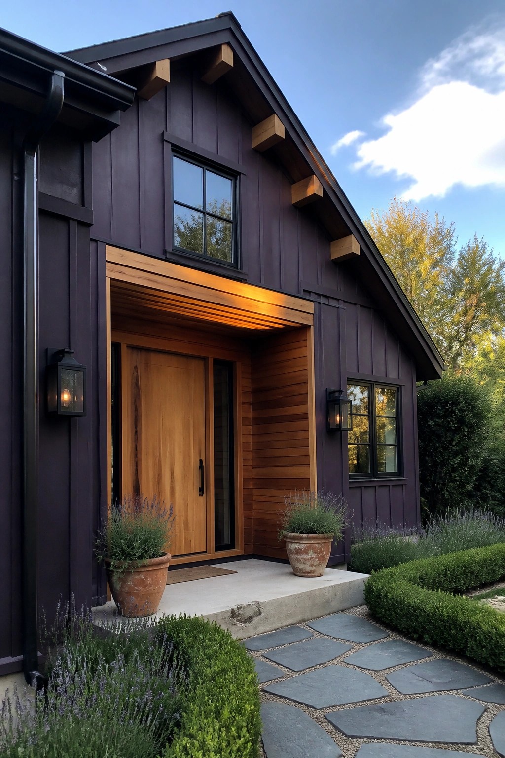 A front view of a house with deep purple siding, natural wood trim around the entry door, two windows, potted plants on the concrete step, and a stone pathway.