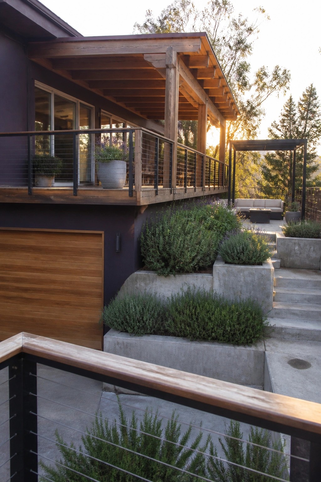 Modern dark house with wooden deck, concrete planters, stairs, and sunset patio