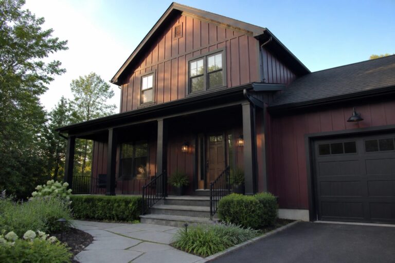 19 Sophisticated Maroon and Black House Exteriors Built Around Matte Black Trim A two-story maroon house with matte black trim on windows, porch columns, railings, and garage door, plus a stone walkway leading to the front steps.