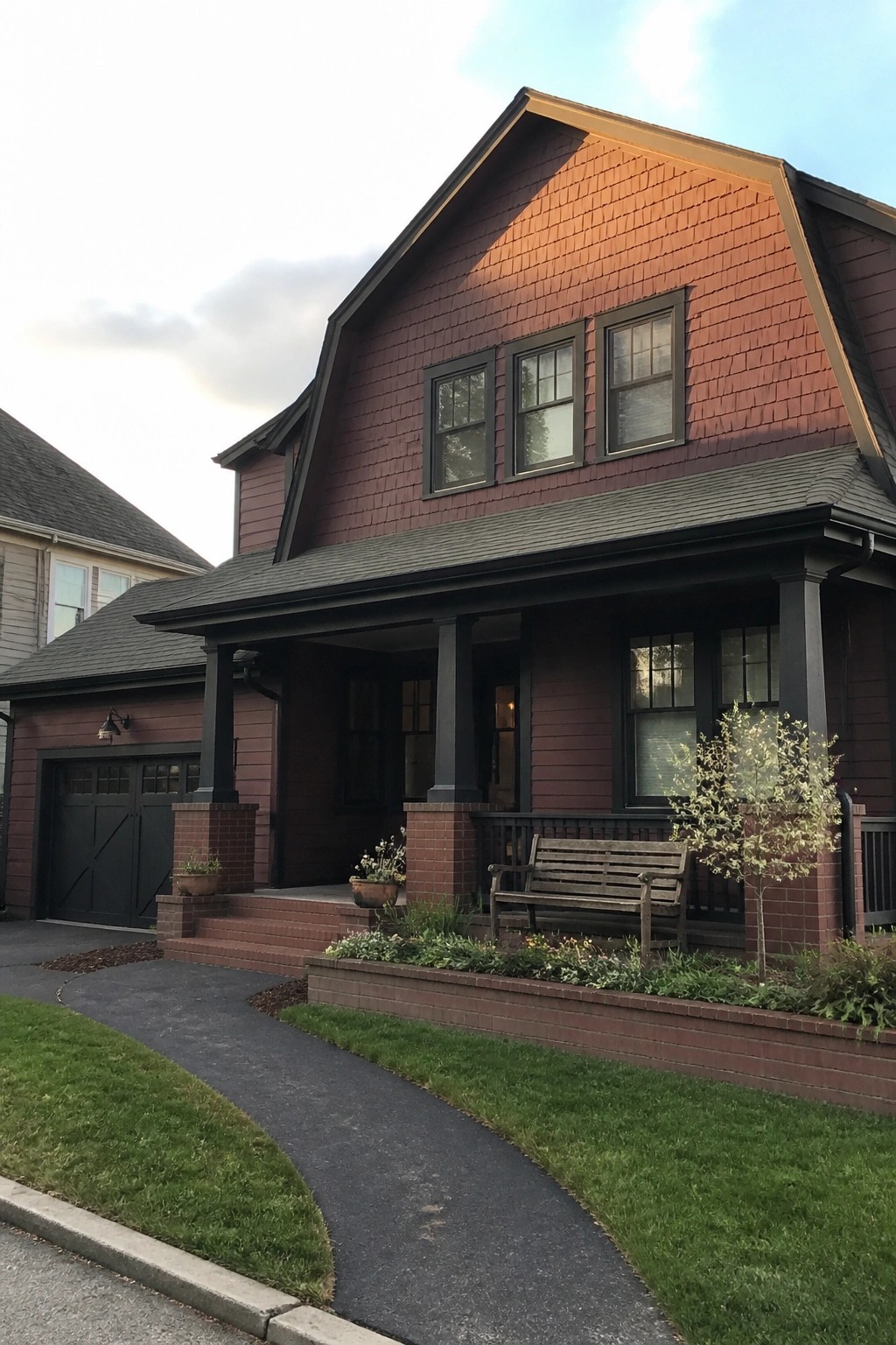 A two-story maroon house with matte black trim, a gabled roof, and a covered front porch with brick columns.