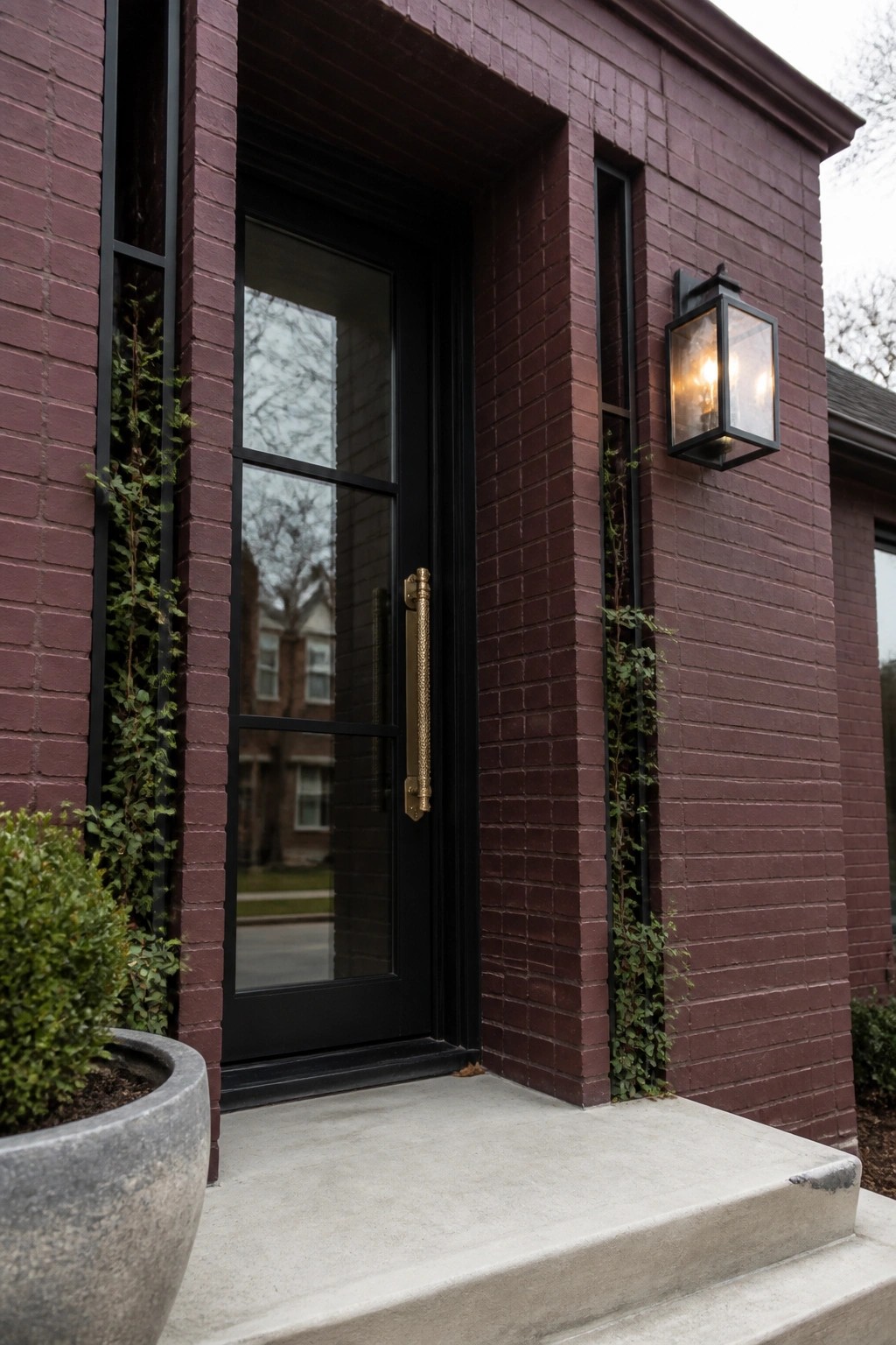 Front entrance of a maroon brick house showing a black door with grid glass panels, black trim, a brass handle, and a black wall lantern.