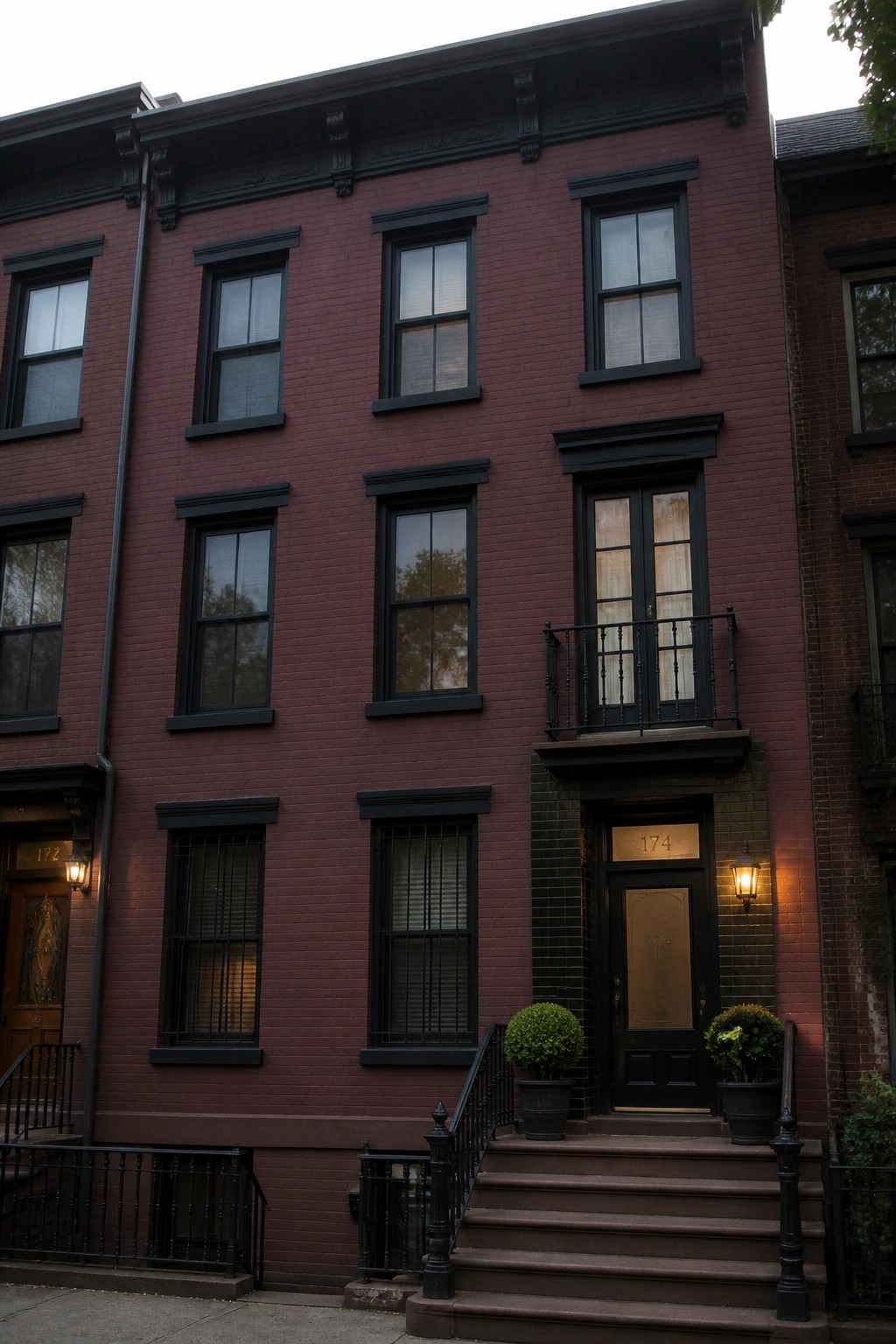 A red brick row house exterior with matte black window frames, a black door marked 174, black railings, and steps leading to the entrance.