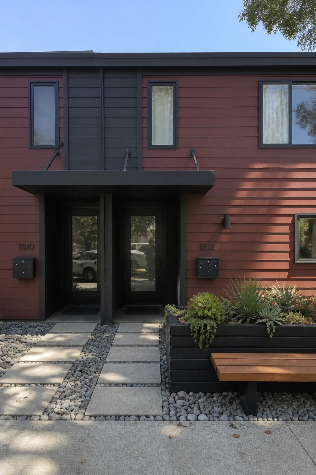 Modern red building with black double doors, planter bench, and gravel walkway.