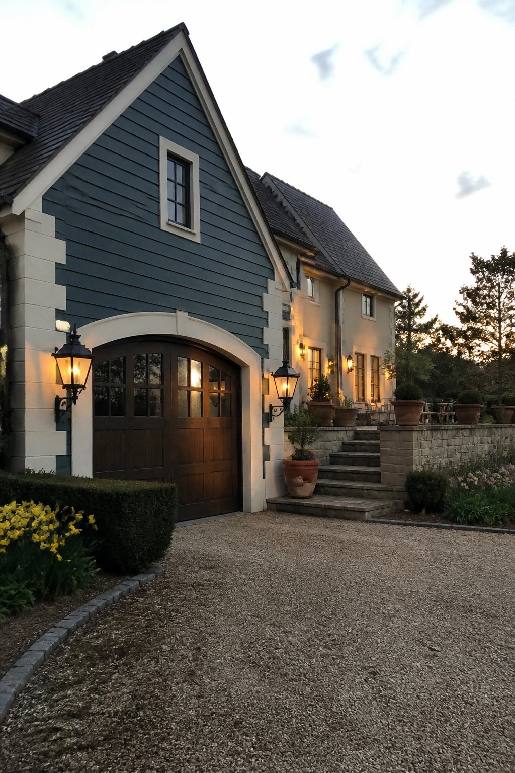 A house exterior featuring deep teal lap siding, white trim, stone corner blocks, and a wooden arched garage door.