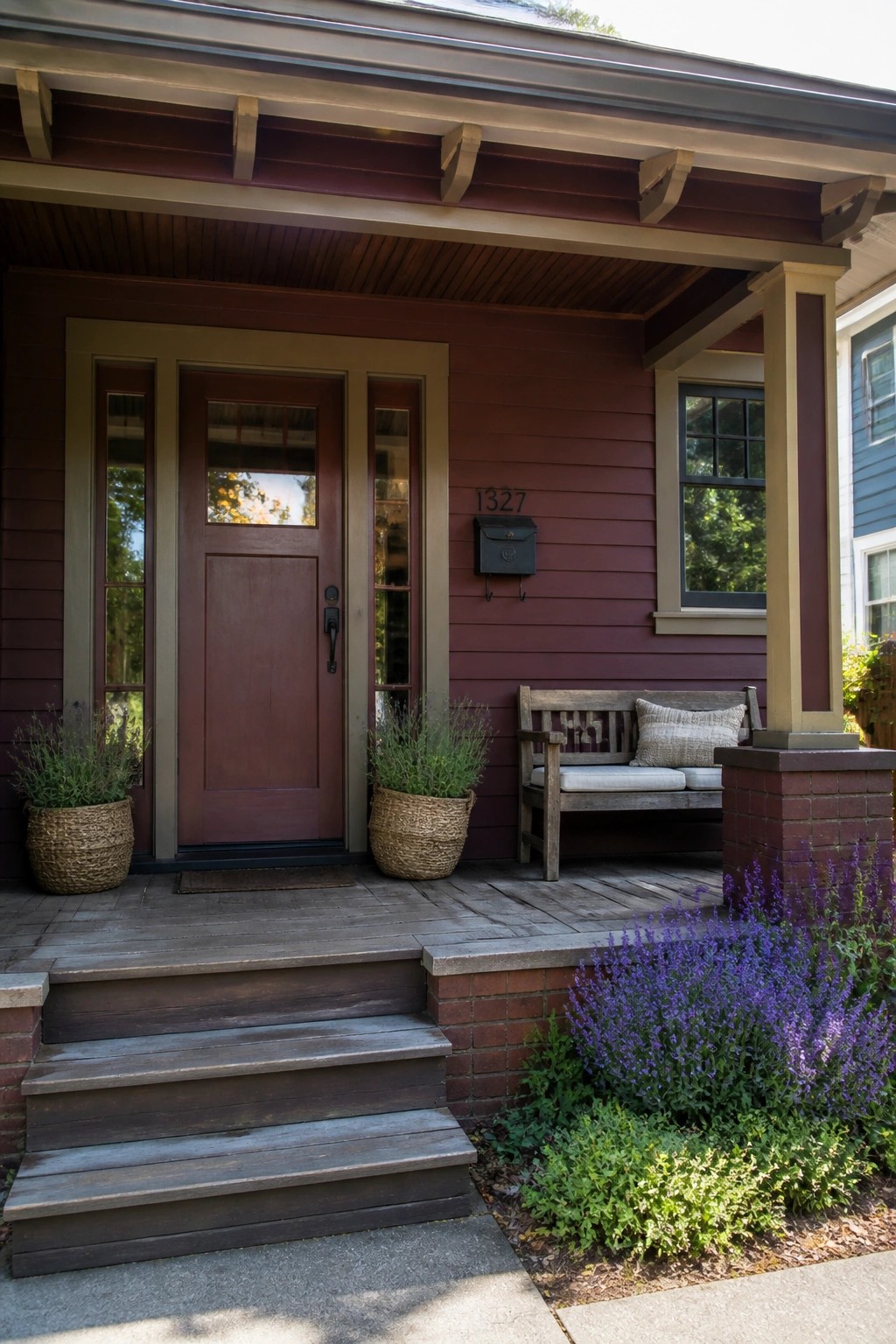 A burgundy house exterior with a wood porch, bench, steps, and potted plants beside the front door.