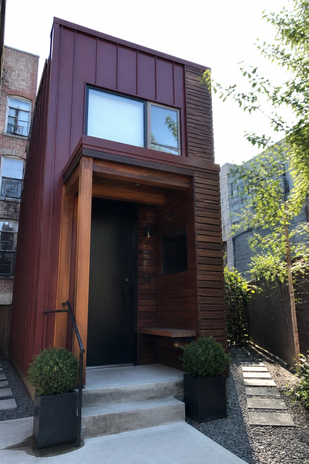 Modern red metal tiny house with black door, wooden trim, and potted plants