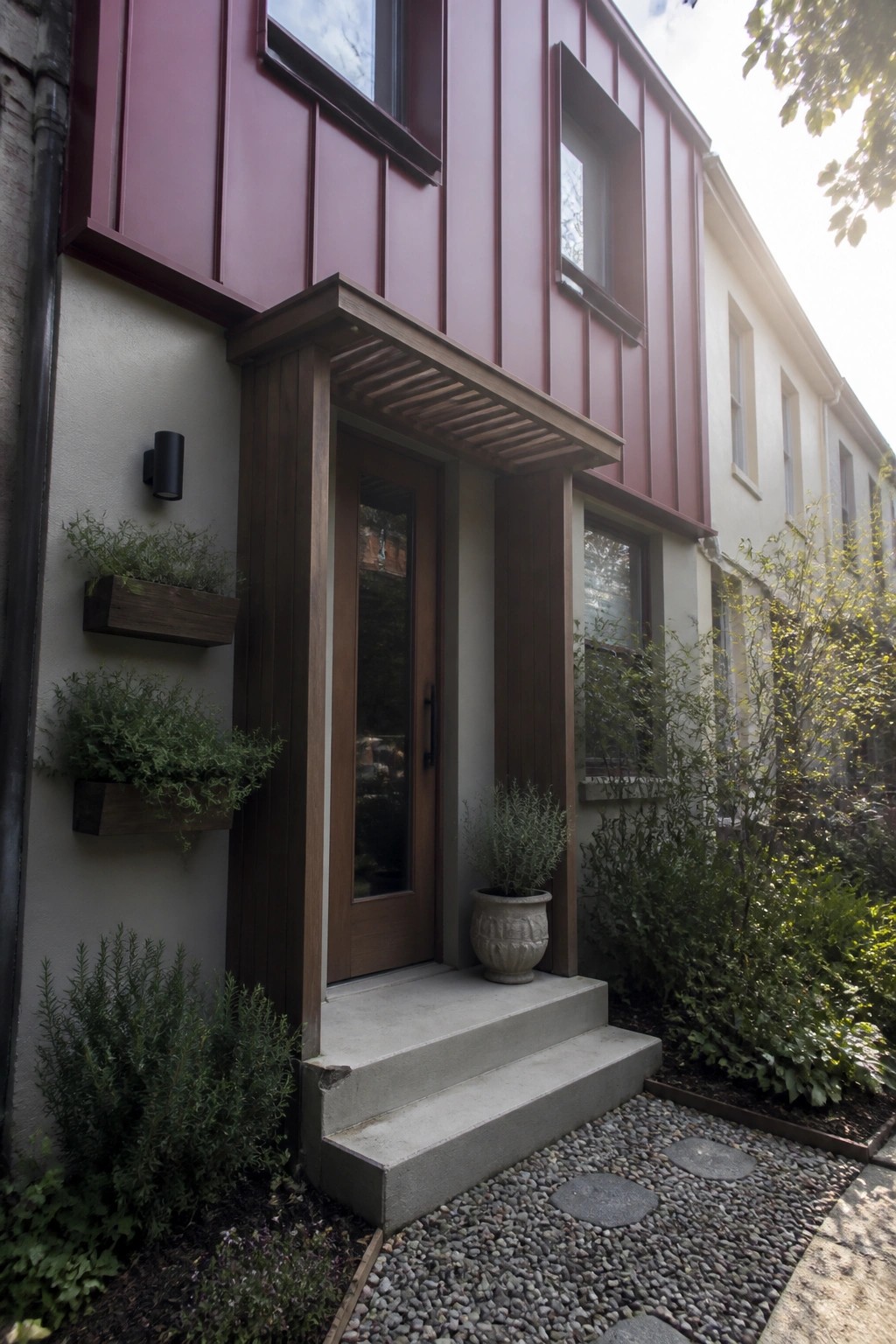 Maroon-sided home entrance with wooden door, canopy, concrete steps, and gravel path.