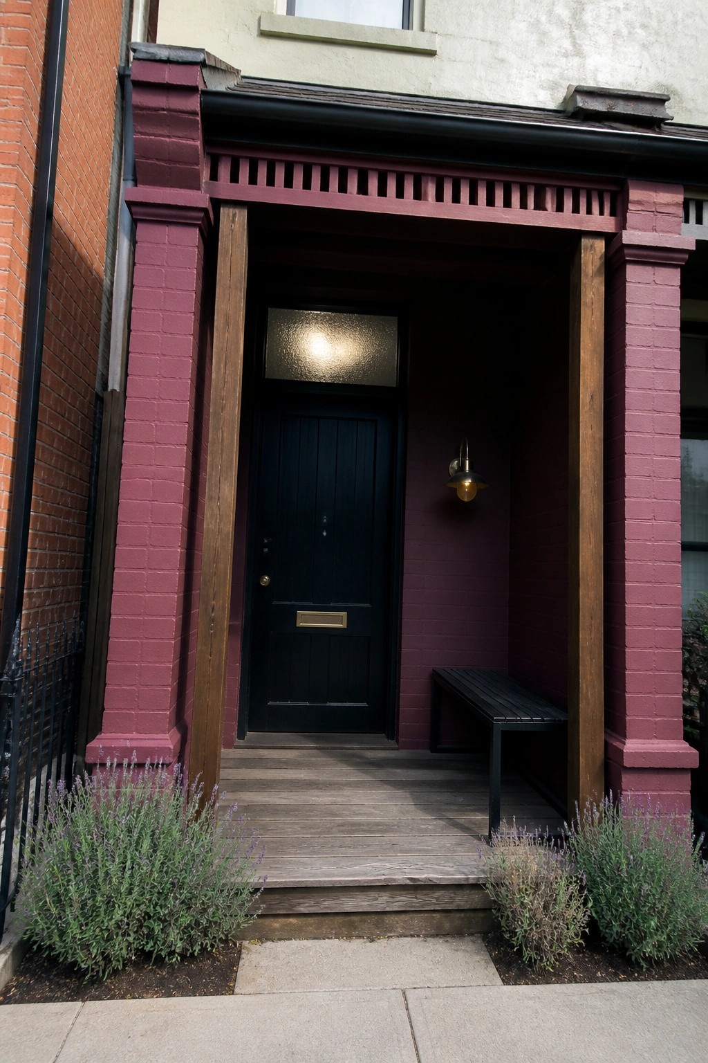 Black door in maroon brick alcove with bench, light, and lavender plants