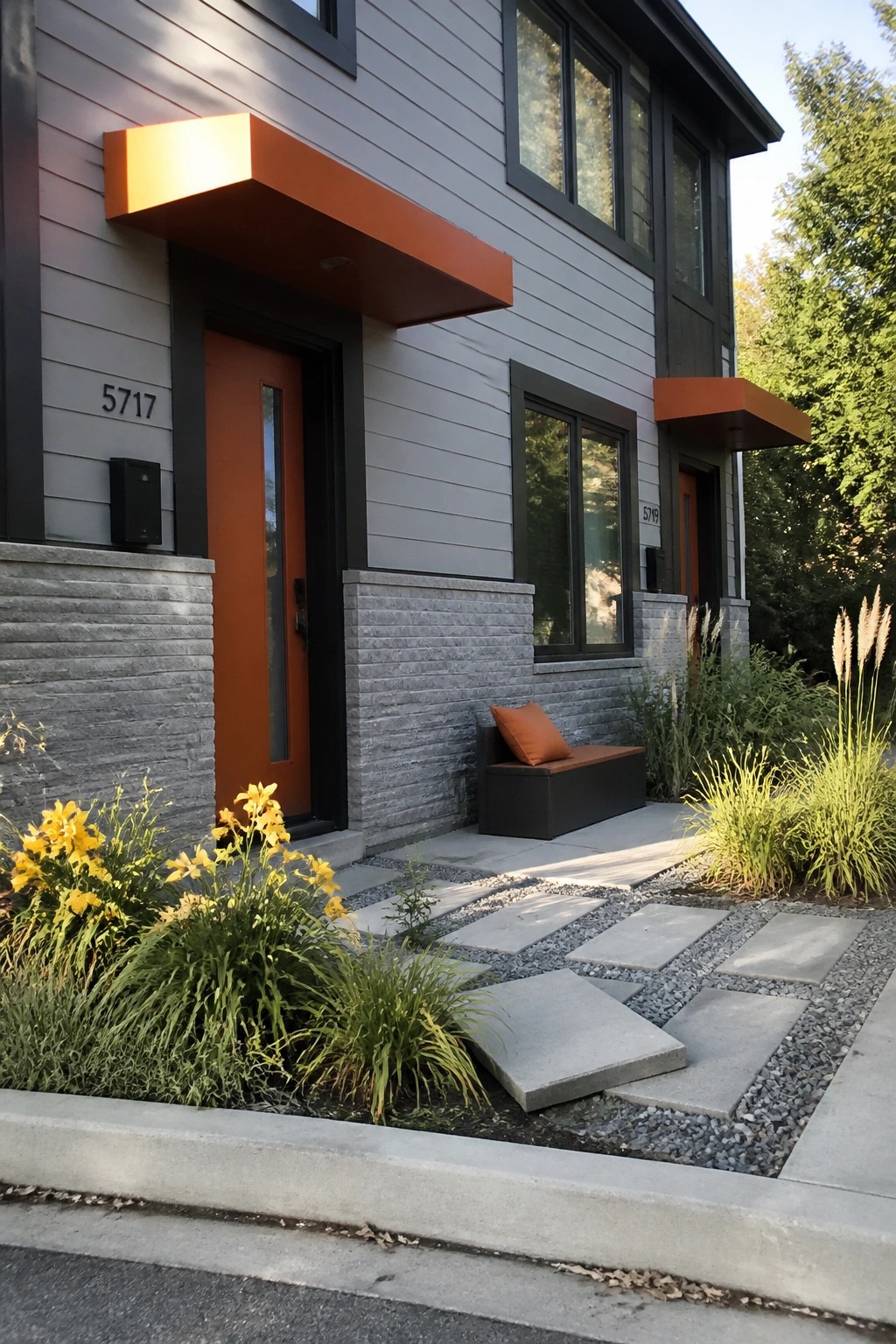 Modern gray townhomes with orange doors, awnings, yellow flowers, and stone path.