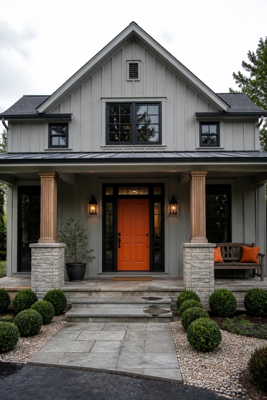 Gray house with bright orange door, stone porch pillars, and shrub-lined steps.