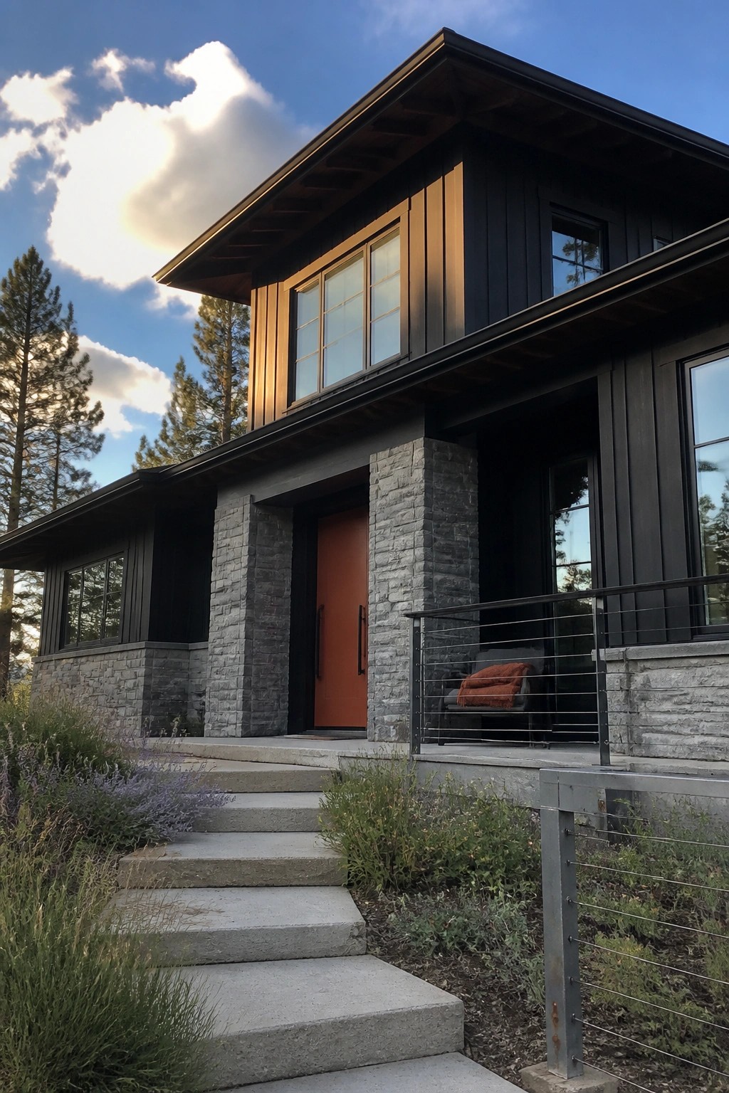 A modern two-story house with dark siding, gray stone pillars, an orange front door, and concrete steps leading up to the entry.