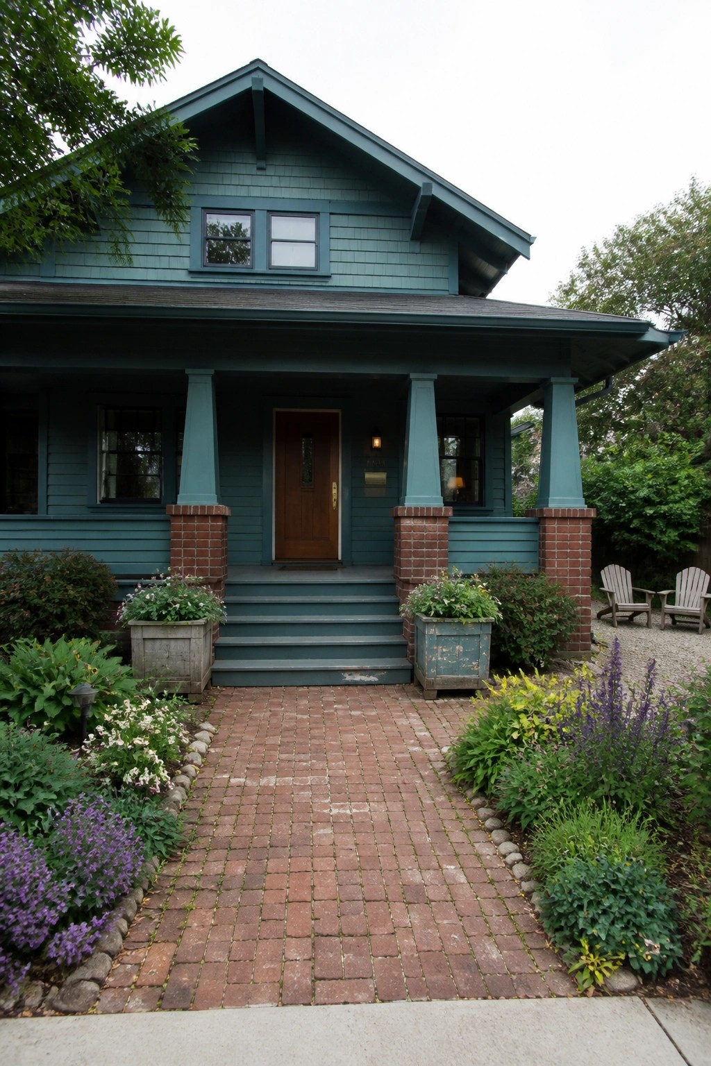Front view of a teal Craftsman house with a covered porch, tapered columns on brick piers, a centered wooden door, and a red brick walkway leading to the steps.