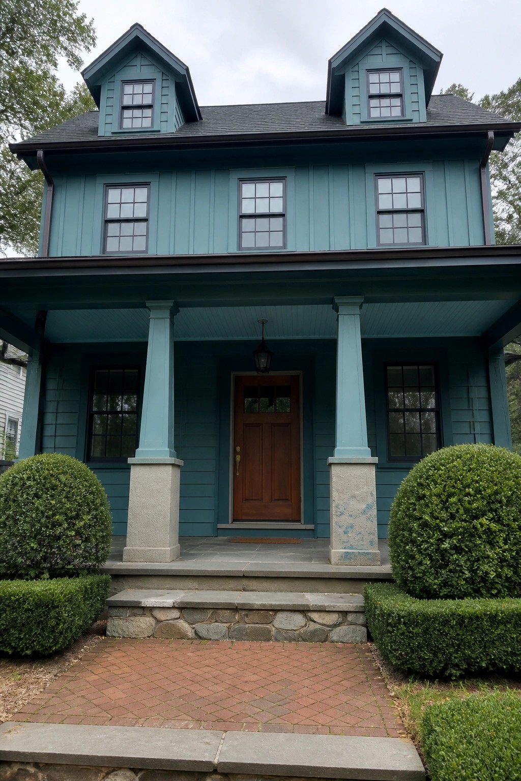 Teal two-story house with dormers, brown door, porch columns, and brick path