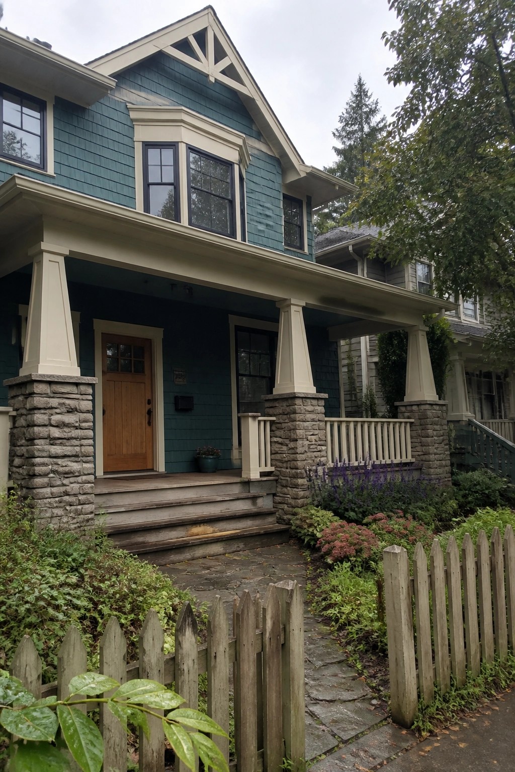 A teal Craftsman house exterior showing a front porch with tapered columns on stone bases, a wooden door, and stone pathway.