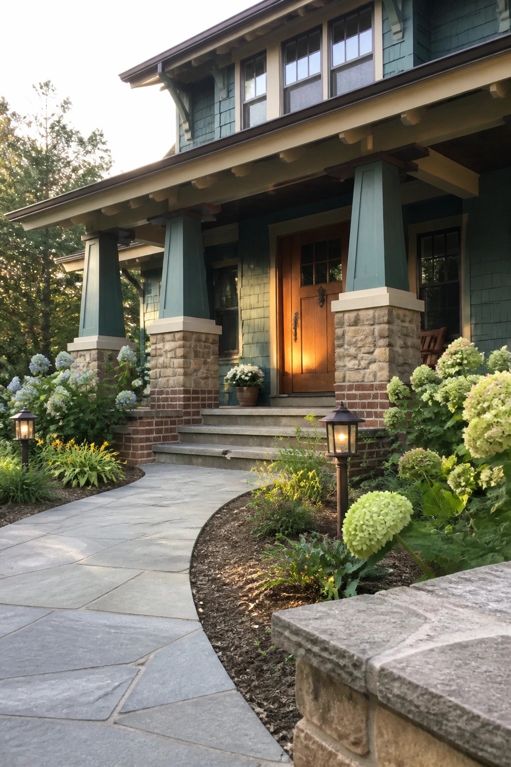 Front view of a teal Craftsman house porch with tapered columns resting on stone and brick piers, a wooden front door, and a curving stone walkway.
