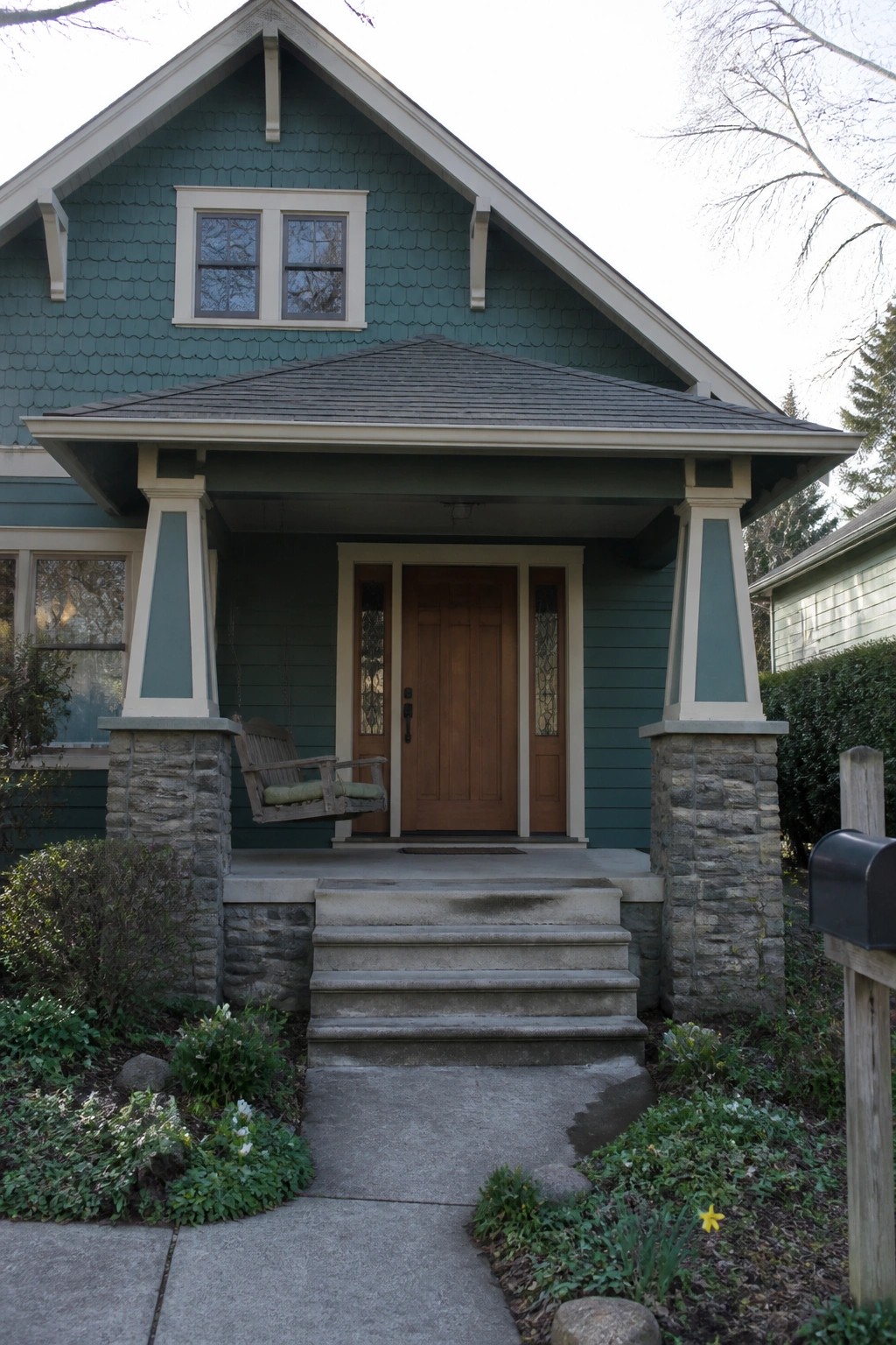Front view of a teal Craftsman house with a covered porch supported by tapered columns on stone piers.