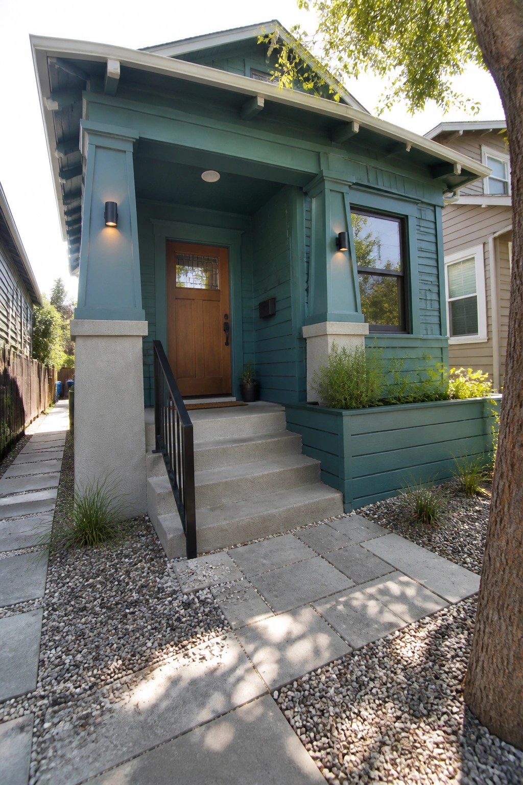 Front view of a teal Craftsman house with a covered porch supported by tapered columns that have concrete bases, concrete steps, and a wooden front door.