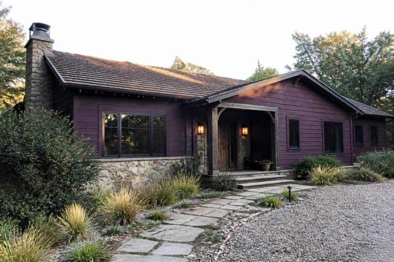 22 Cozy Purple Ranch House Exteriors Featuring Plum Siding and Stone Accents A single-story ranch house with plum siding, a tall stone chimney, a wooden front door under a small covered porch, and a winding stone path through the front yard.