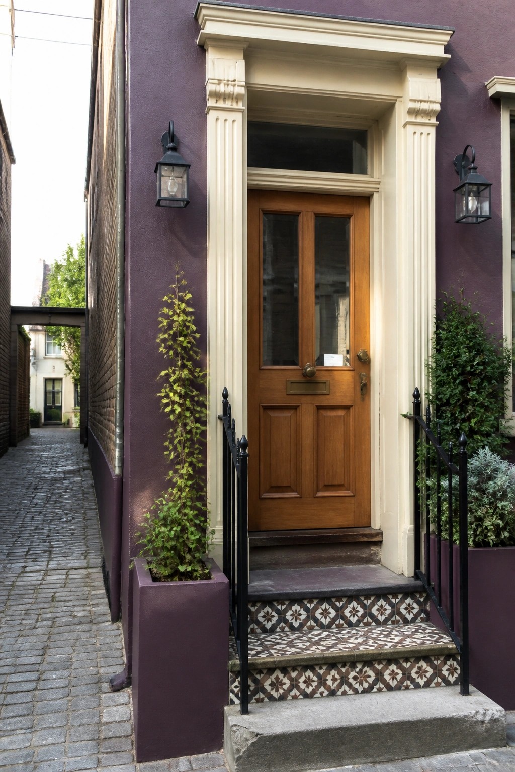 A wooden front door with glass panes set inside cream trim and columns on a plum purple exterior wall, with tiled steps and black railings.
