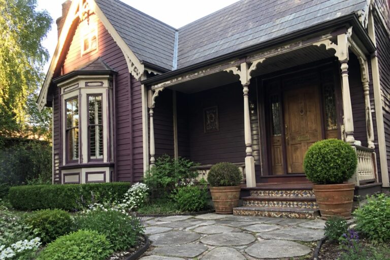 20 Dramatic Plum House Exterior Ideas Using Cream Trim Purple Victorian house with ornate porch, stone path, potted shrubs, and garden
