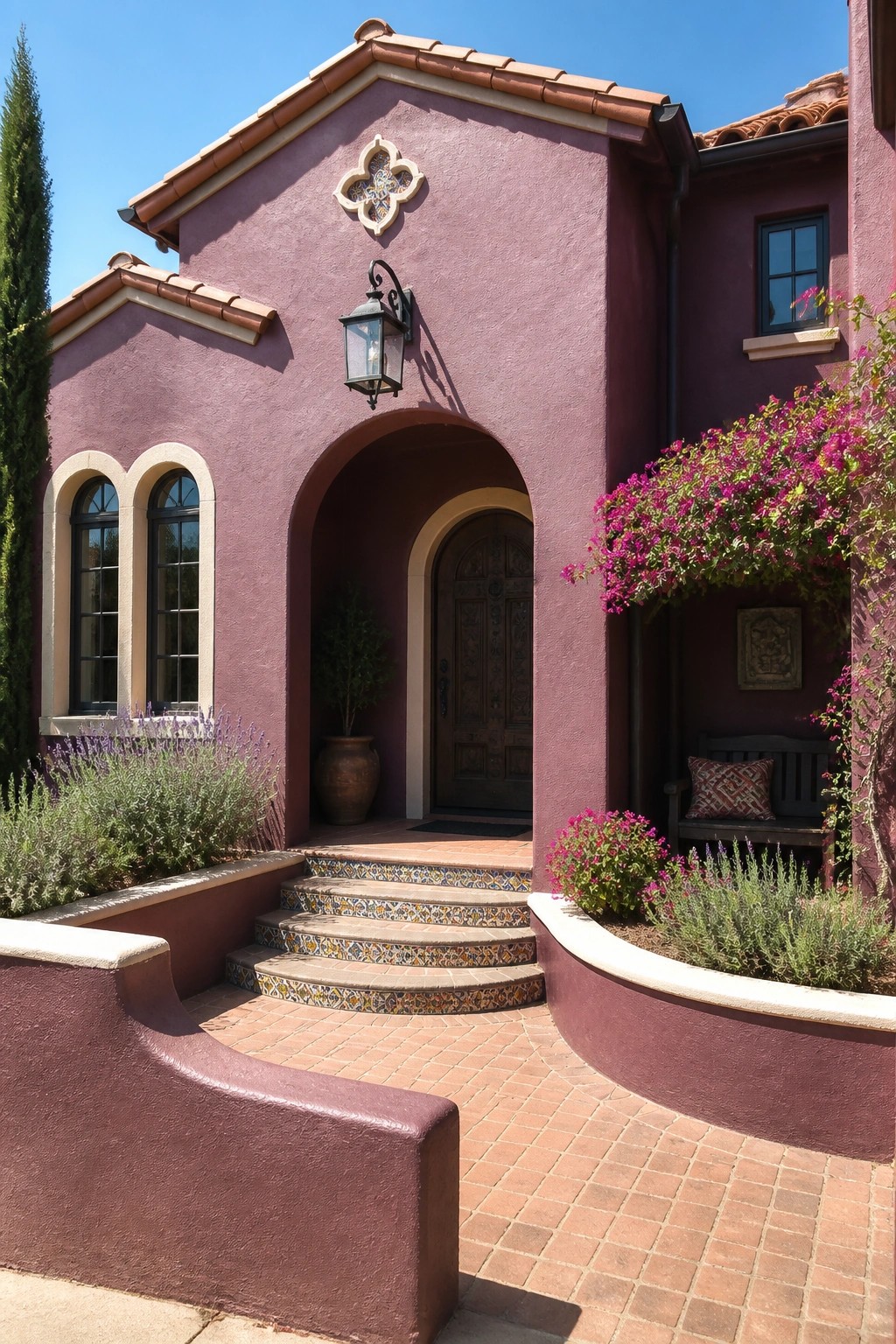 A plum stucco house with cream trim around arched windows and an arched entryway, terracotta roof tiles, and a dark wooden door.
