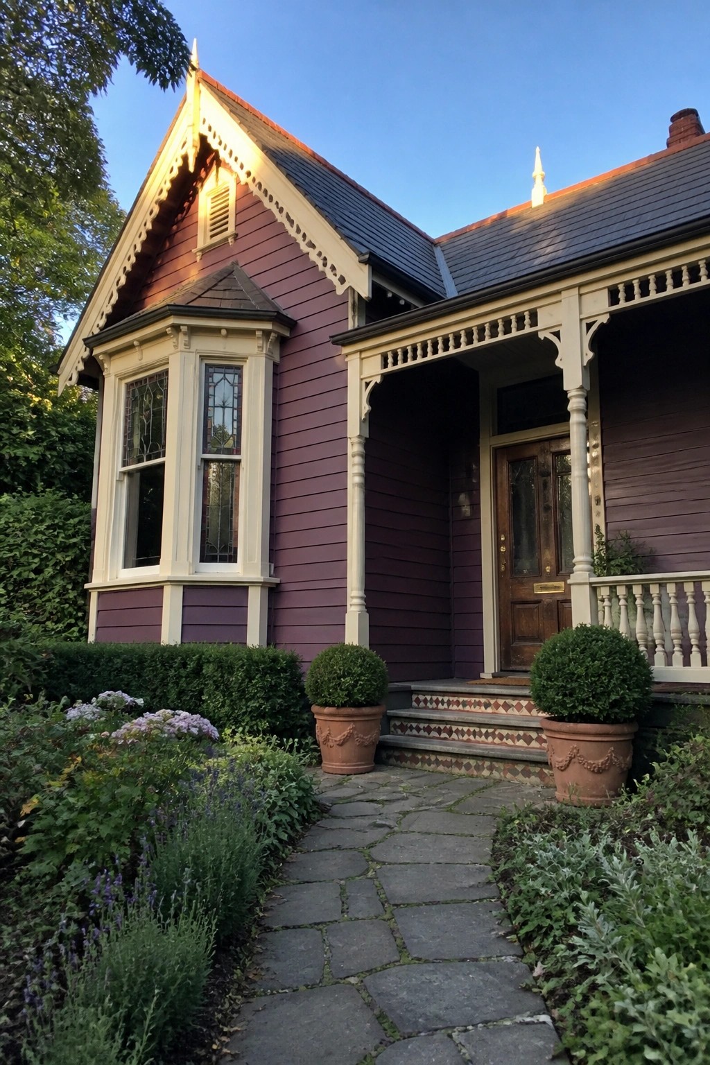 Purple Victorian house with ornate porch, stone path, potted shrubs, and garden