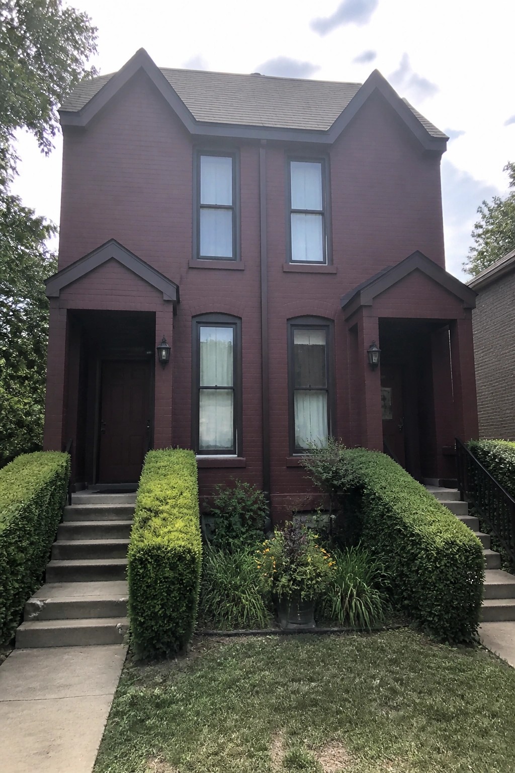 Red brick duplex with two entrances, windows, and lush green landscaping.