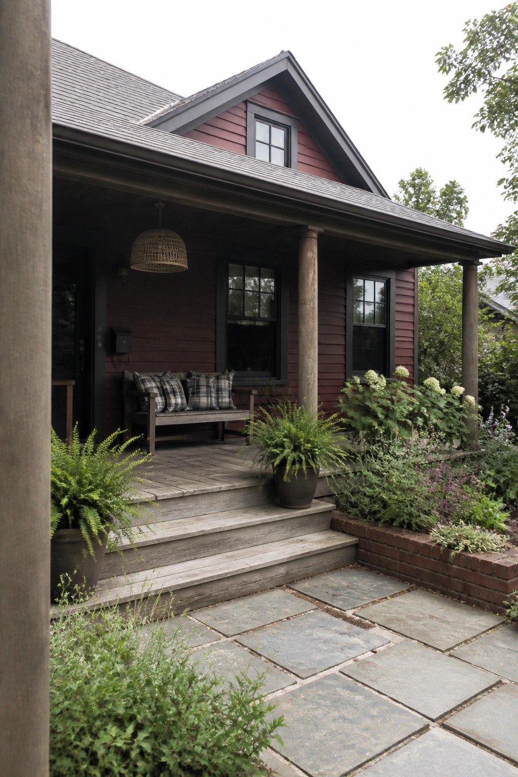 A maroon house with dark trim, a gray roof, a wooden porch, and a stone path leading to the front steps.