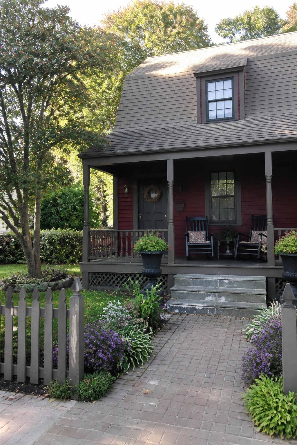Red house with gray porch, rocking chairs, and flower pots along brick path