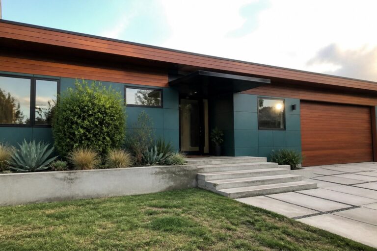 A modern teal house exterior featuring smooth fiber cement panels, a wooden garage door, black-framed windows, and concrete steps leading to the front entry.
