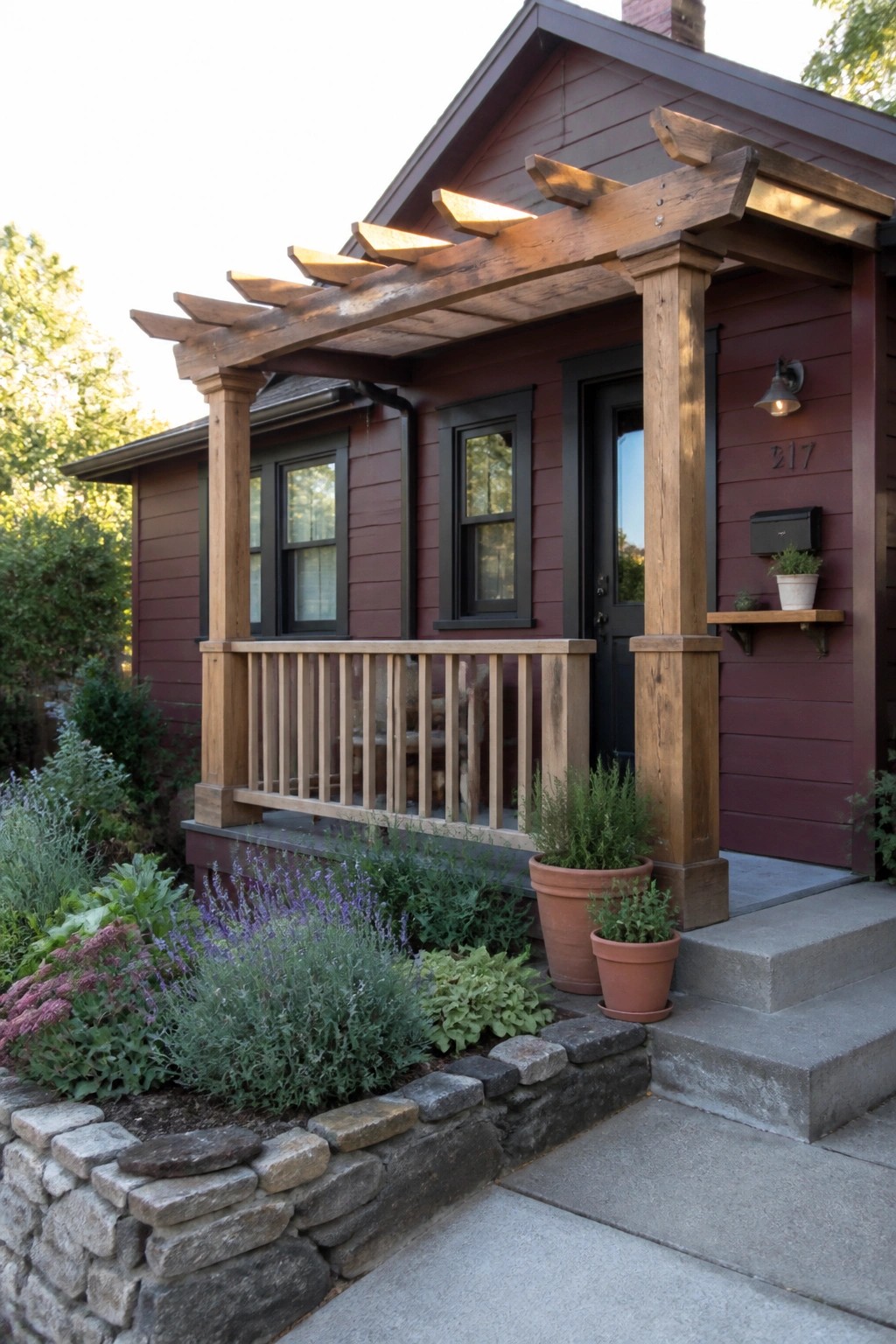 A burgundy house exterior with a wooden pergola, porch posts, and railing over concrete steps and potted plants.