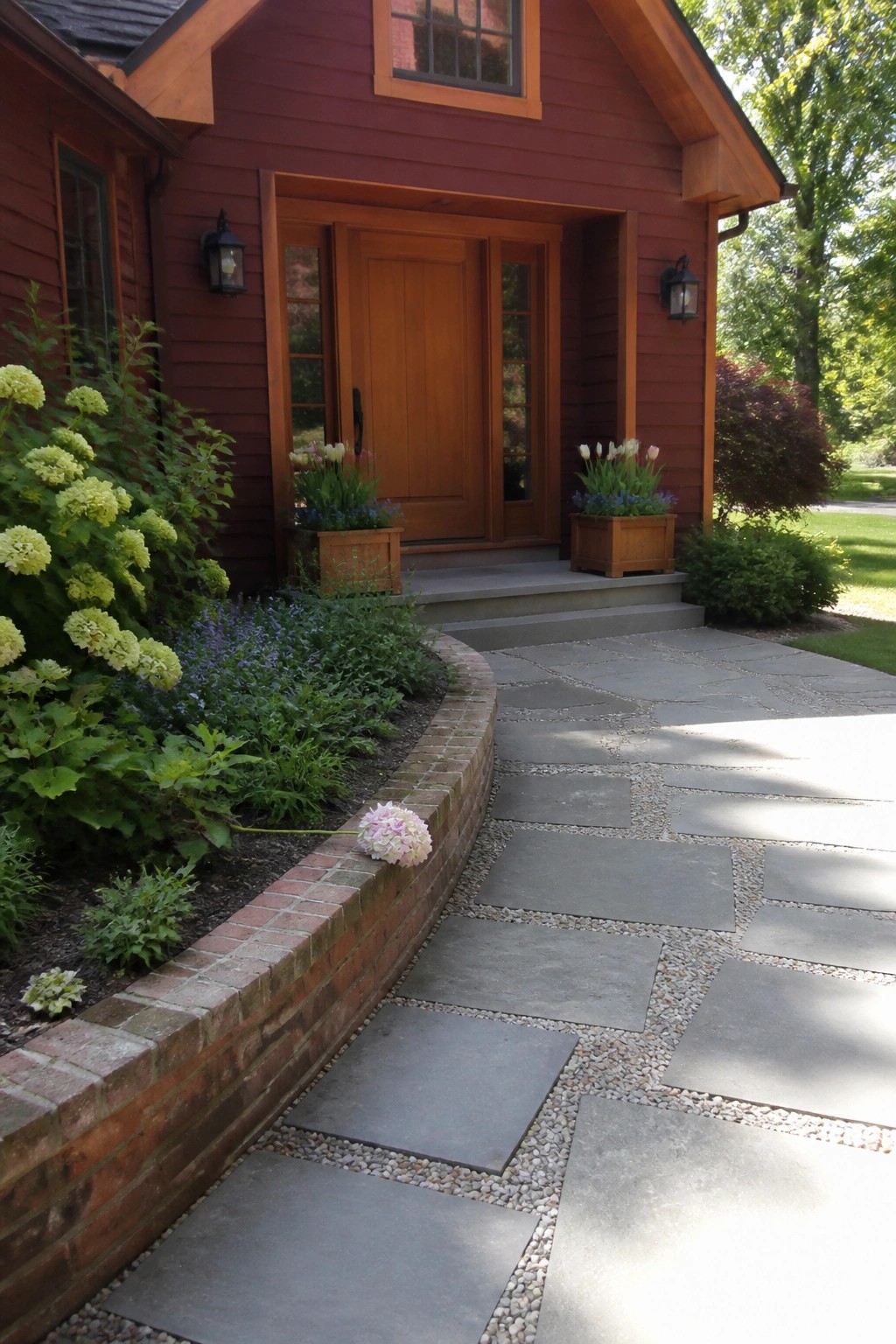 Front view of a burgundy house exterior featuring a wooden front door, cedar trim, stone pathway, and landscaped flower beds.