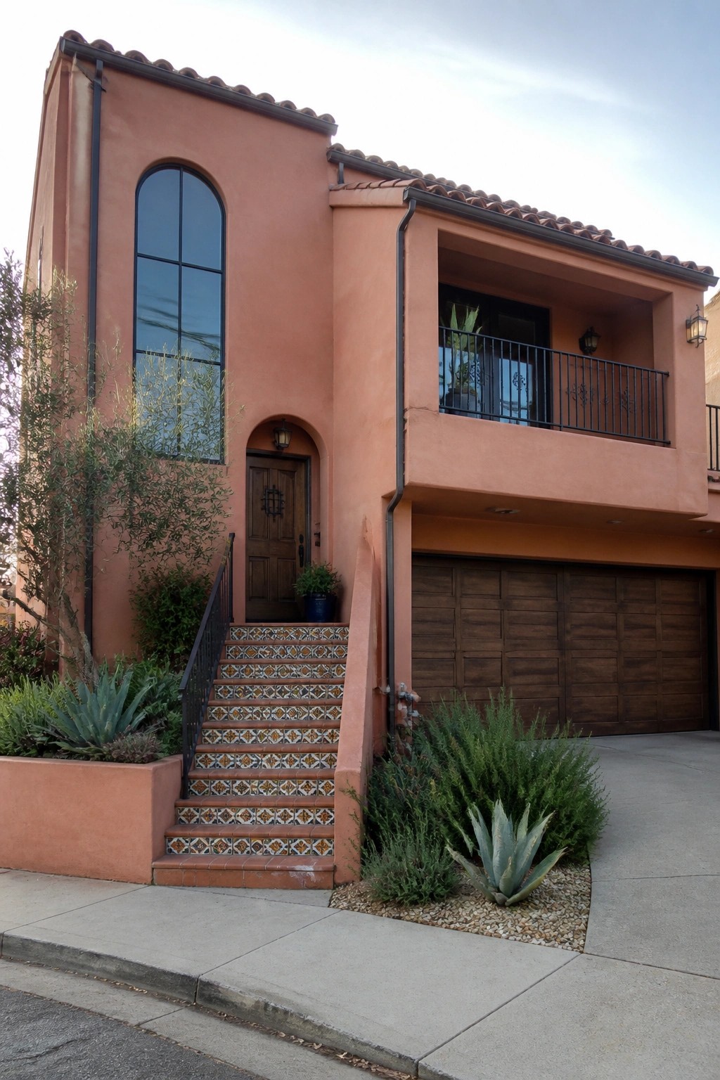 Peach stucco two-story house with arched entry, tiled stairs, balcony, and garage