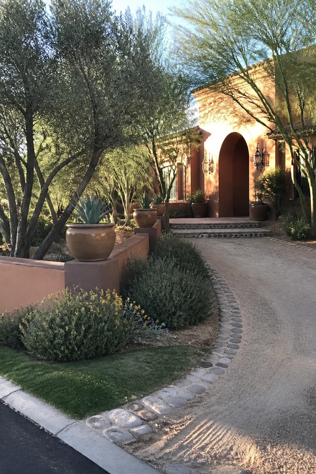 Southwestern adobe home with arched entry, terracotta pots, and curving desert driveway